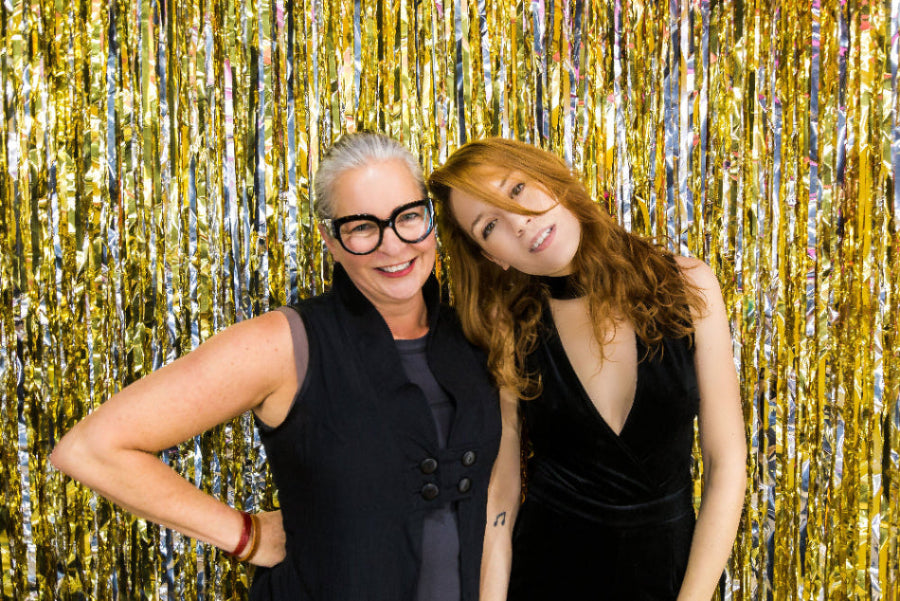 Zwei Frauen vor einer golde schimmernden Wand während einer Modenschau