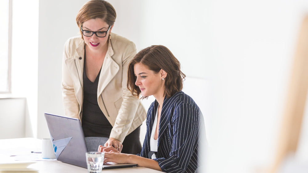 Zwei Frauen in weißem Zimmer arbeiten an Laptop