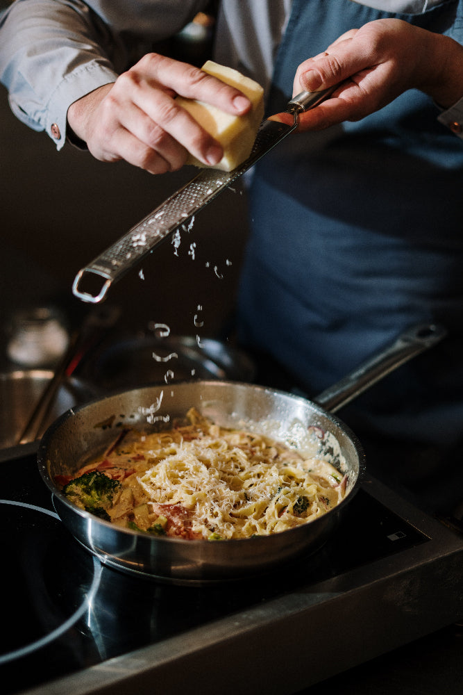 Parmesan wird auf Gemüsepfanne gerieben in der Küche des PLICANA