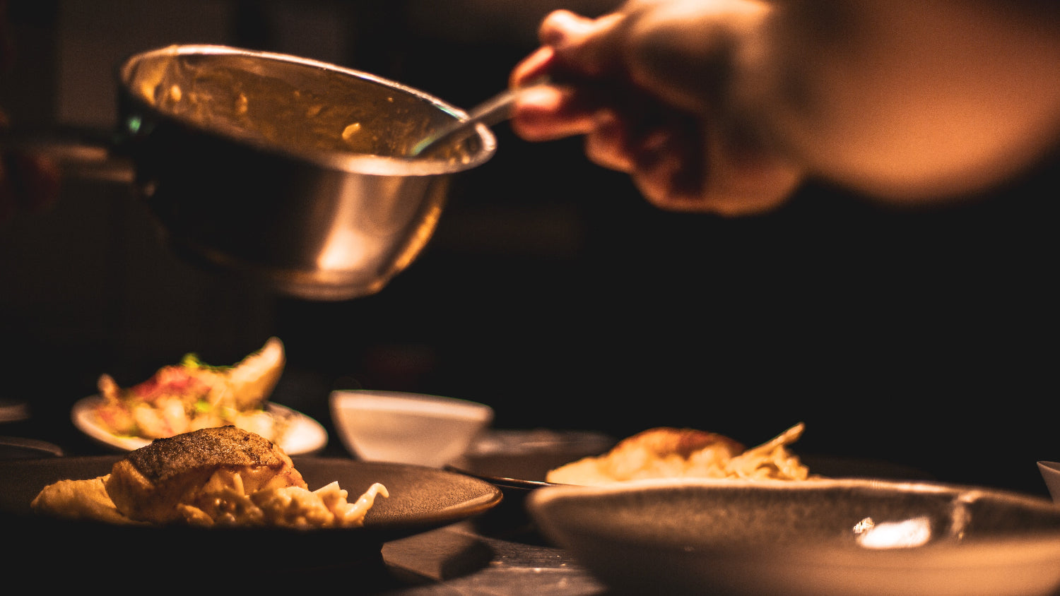 Soße wird auf Essen in schwarzen modernen Tellern gegossen